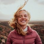 A blonde young lady standing outside enjoying feeling the the wind in her face.