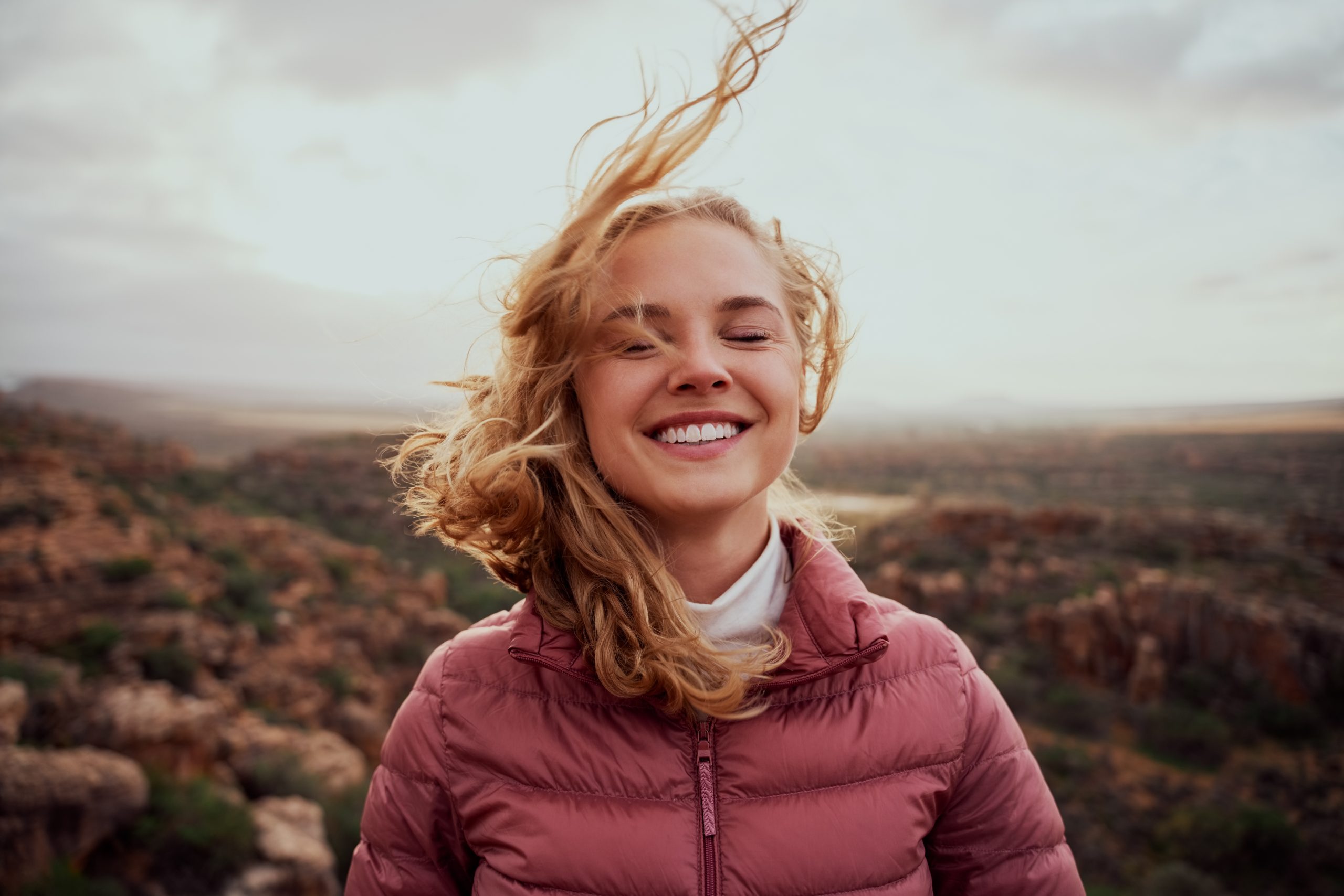 A blonde young lady standing outside enjoying feeling the the wind in her face.